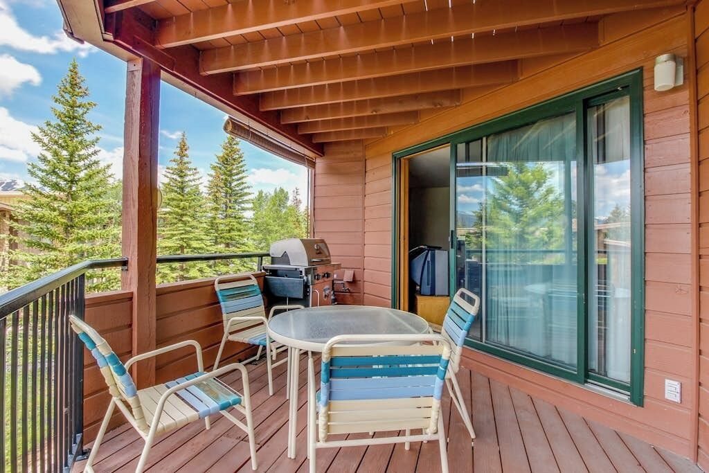 A wooden deck with a table and chairs, a grill, and a sliding glass door.