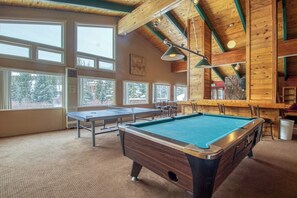 Ein Billardtisch, Billiardkugeln und eine Bar in einem Raum mit großen Fenstern und Holzbalken.