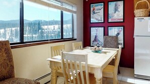 Un comedor con mesa y sillas, vistas a un paisaje nevado a través de amplios ventanales y un refrigerador.