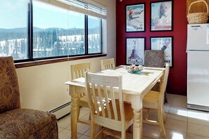 Ein Essbereich mit Tisch und Stühlen, mit Blick auf eine verschneite Landschaft durch große Fenster, sowie ein Kühlschrank.