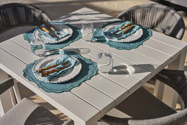 A table set with plates, cutlery, and glasses, surrounded by wicker chairs.