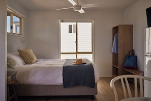 Ein Schlafzimmer mit Bett, Deckenventilator, Fenster, Kleiderschrank und Sessel.