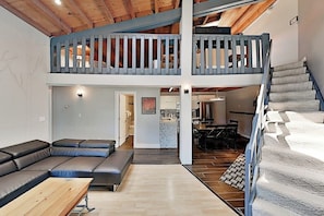 Ein geräumiger Wohnbereich mit hoher Decke, einer Holztreppe und einem Balkon mit Geländer.