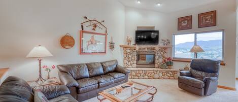 A living room with a leather sofa, a glass coffee table, a stone fireplace, a television, and a large window with a view.
