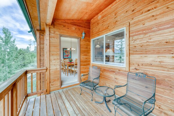 Eine Holzhütte mit Balkon, zwei Metallstühlen, einem Tisch und einer Tür, die in einen Innenraum mit einem Esstisch und Stühlen führt.