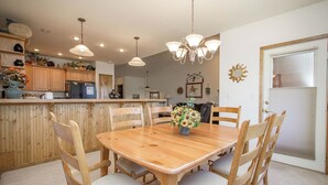 Un coin repas avec une table et des chaises en bois, un lustre et une cuisine en arrière-plan.