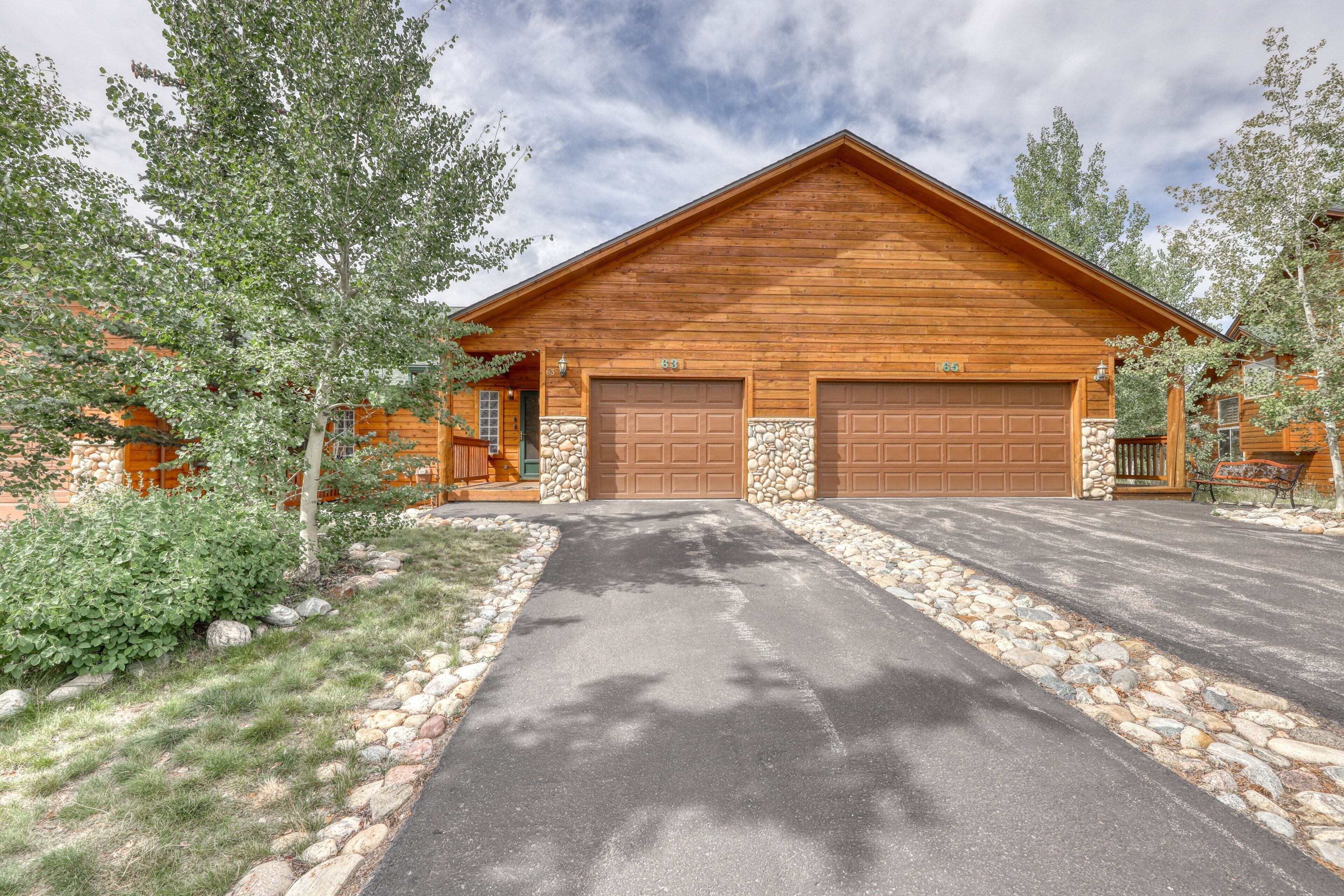 A two-story wooden building with a stone foundation, two garage doors, and a paved driveway.