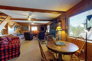 Ein gemütliches Blockhaus-Interieur mit Kamin, Holzbalken, Esstisch und einer Couch.