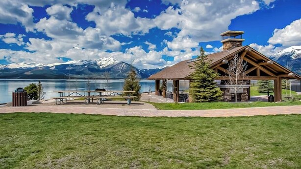 Un lodge con un camino in pietra, tavoli da picnic e vista sulle montagne e sul lago.