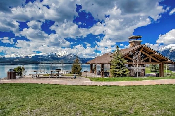 A lodge with a stone chimney, picnic tables, and a view of mountains and a lake. - Cozy condo in great location - access to shared pool & game room (Dillon)