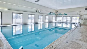 Una piscina interna con ampie finestre, pavimento piastrellato e ringhiera in metallo.