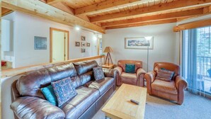 Eine Holzbalkendecke, ein Ledersofa, ein Couchtisch aus Holz und ein Sessel mit Kissen.