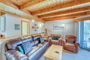 Eine Holzbalkendecke, ein Ledersofa, ein Couchtisch aus Holz und ein Sessel mit Kissen.