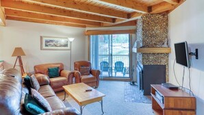 Ein gemütliches Wohnzimmer mit Holzbalkendecke, einem Steinofen, einem Sofa, einem Couchtisch und einem Fernseher.