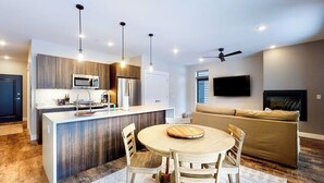 A modern kitchen with a central island, dining area with chairs, a sofa, and a ceiling fan. - Modern riverfront condo w/ a gas fireplace, washer/dryer & private patio (Silverthorne)