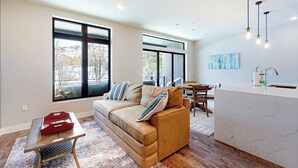 A modern living room with a sofa, a dining area, and a kitchen counter. - Modern riverfront condo w/ a gas fireplace, washer/dryer & private patio (Silverthorne)