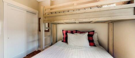 Un lit superposé avec une tête de lit blanche et un lit inférieur recouvert d’une courtepointe blanche matelassée.