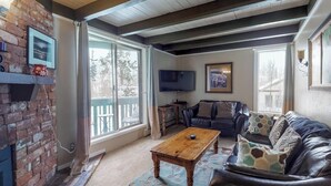 A living room with a fireplace, a leather sofa, a coffee table, and a television. - Family-friendly condo w/ shared pool, hot tub, game room, & fitness room (Silverthorne)