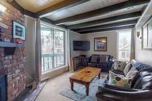 A living room with a fireplace, a leather sofa, a coffee table, and a television. - Family-friendly condo w/ shared pool, hot tub, game room, & fitness room (Silverthorne)