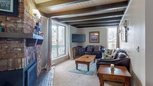 A living room with a fireplace, a sofa, a coffee table, and a television. - Family-friendly condo w/ shared pool, hot tub, game room, & fitness room (Silverthorne)