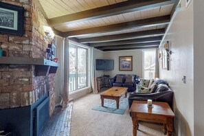 A living room with a fireplace, a sofa, a coffee table, and a television. - Family-friendly condo w/ shared pool, hot tub, game room, & fitness room (Silverthorne)