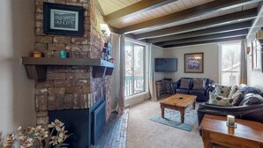 A living room with a brick fireplace, a couch, a coffee table, and a television. - Family-friendly condo w/ shared pool, hot tub, game room, & fitness room (Silverthorne)