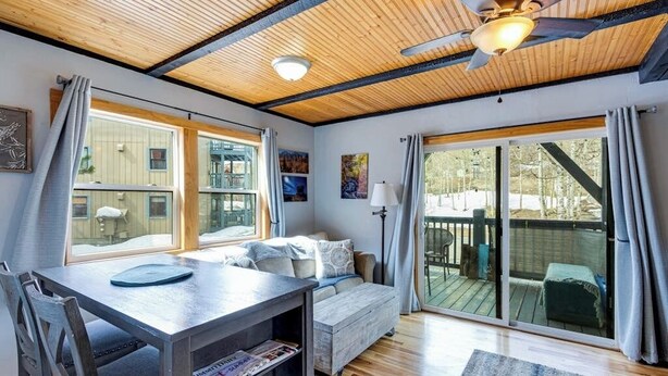 Una habitación acogedora con techo de madera, una cama, una mesa de comedor con sillas y ventanas grandes.
