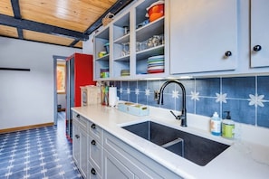 Eine Küche mit weißer Arbeitsplatte, einem schwarzen Spülbecken und einer blau-weißen Spritzschutzwand.