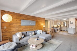 Ein modernes Wohnzimmer mit einem Ecksofa, einem runden Couchtisch und einer Wand im Holzoptik.