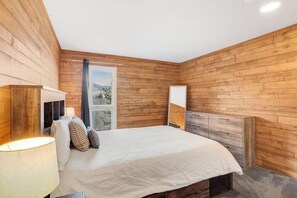 Ein Schlafzimmer mit Holzwandverkleidung, einem Bett mit weißer Bettdecke, einem Nachttisch mit Lampe und einem Fenster mit Blick.