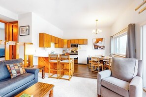 Eine moderne Küche mit Holzausstattung, einem Essbereich mit Tisch und Stühlen, einer Couch und einem Fenster mit Vorhängen.