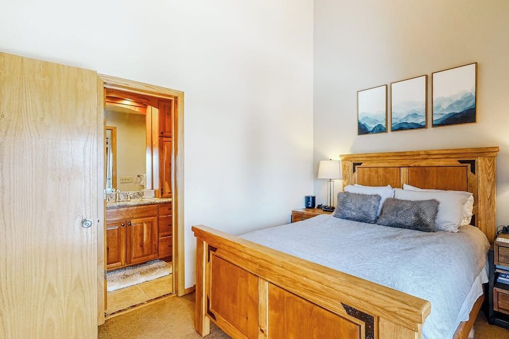 A bedroom with a wooden bed, a nightstand, a lamp, and a wall-mounted picture.