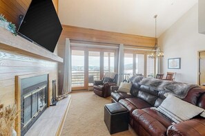 Ein Wohnzimmer mit Kamin, Ledersofa und großem Fenster mit Aussicht.