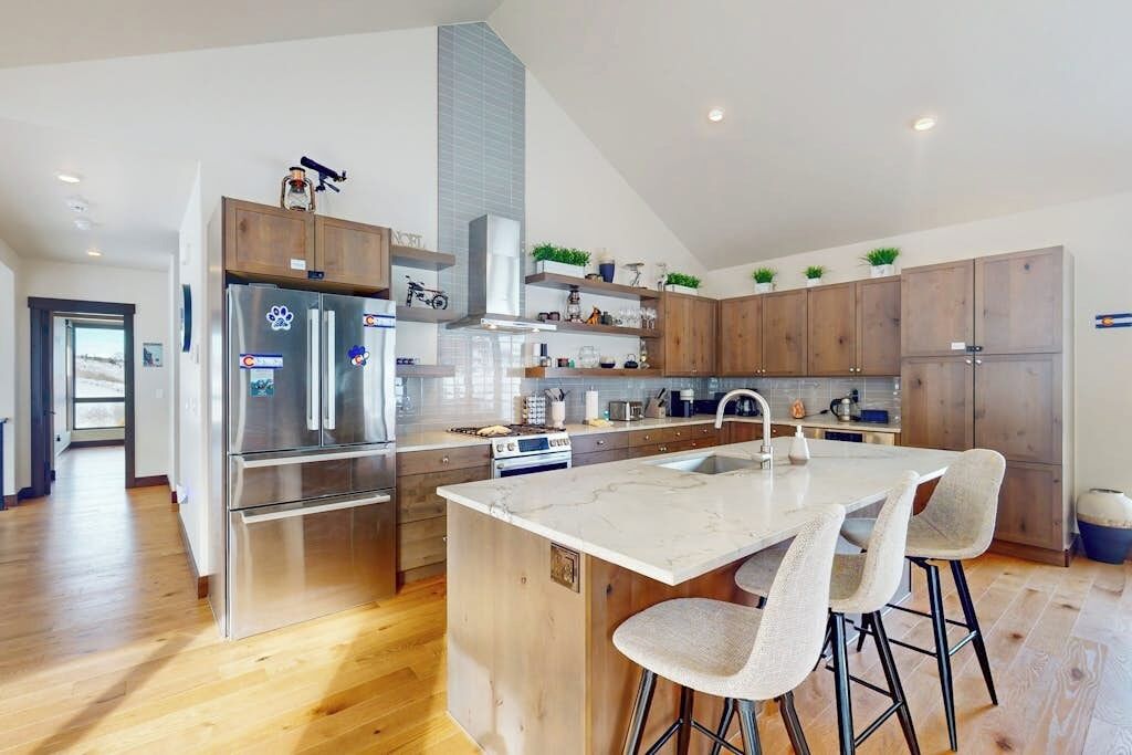 A modern kitchen with a central island, stainless steel appliances, wooden cabinets, and a large window.