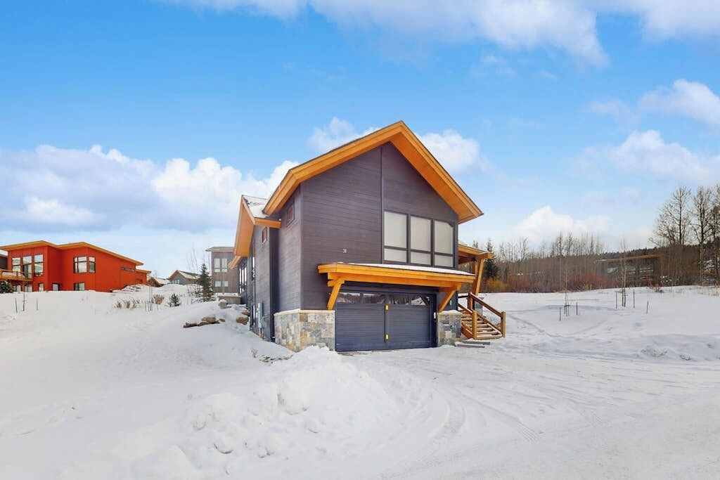 Uma casa moderna com garagem, grandes janelas e paisagem coberta de neve.