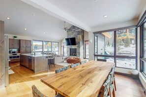 A spacious kitchen with a large island, a dining area with a wooden table, and large windows offering a view of a snowy landscape. - Luxury home with radiant heated floors & private Bullfrog hot tub (Silverthorne)