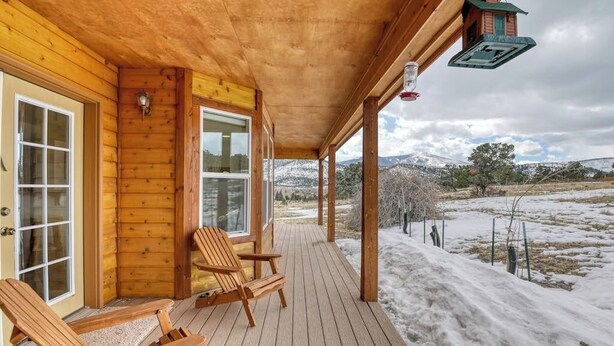 A wooden deck with two chairs, a covered porch, and a view of a snowy landscape. - Hilltop Home w/ Great Mountain Views, Back Porch, WiFi, W/D & Attached Garage (South Fork)