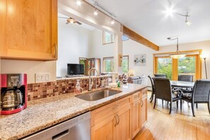 A modern kitchen with granite countertops, wooden cabinets, a built-in dishwasher, and a dining area with a table and chairs. - Mountain House + Loft w/Free WiFi, Enclosed Patio, Gas Grill, Cable (Silverthorne)