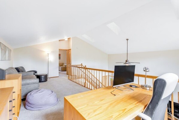 A modern room with a wooden desk, a computer, a chair, a bean bag, a sofa, and a staircase. - Home with loft office, enclosed patio and garage, near the Raven at Three Peaks (Silverthorne)