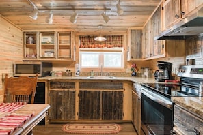 Ein rustikales Blockhaus im Inneren, mit Holzvertäfelung, einer Küchenzeile mit Herd, Mikrowelle und Spüle sowie einem Essbereich mit Tisch und Stühlen.