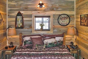 A cabin-style room with a bed, two bedside lamps, a wall clock, a window with a view, and a welcome sign. - Remodeled, Mountain View Cabin w/ Fireplace, Firepit & WiFi - Dogs Welcome (South Fork)