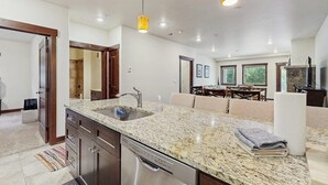 Une cuisine moderne dotée de plans de travail en granit, d’un lave-vaisselle et de luminaires suspendus.