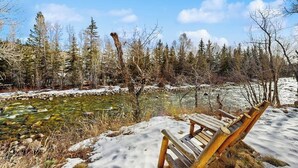 Un banc dans un paysage enneigé, avec un ruisseau aux eaux claires et des arbres en arrière-plan.