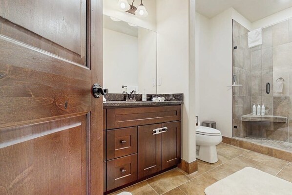 A modern bathroom with a wooden vanity, a glass shower enclosure, and a white toilet. - Riverfront condo with balcony, walking distance to Rainbow Park (Silverthorne)