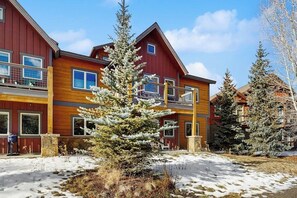 A multi-story building with a red facade, balconies, and a snow-covered ground. - Riverfront condo with balcony, walking distance to Rainbow Park (Silverthorne)