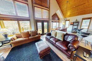 Ein geräumiges Wohnzimmer mit zwei Ledersofas, einem Couchtisch und einem Essbereich mit Tisch und Stühlen. Große Fenster sorgen für natürliches Licht und Ausblick.