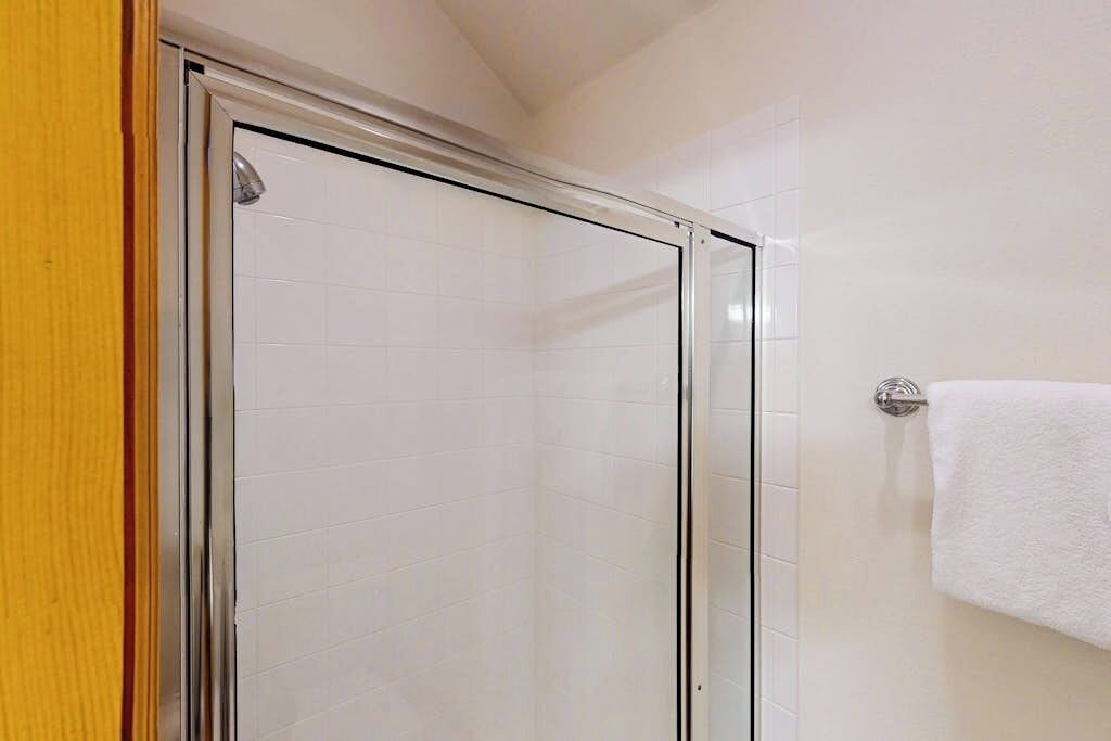 Een badkamer met witte betegelde wanden, een glazen douchecabine en een witte handdoek aan een metalen handdoekrek.