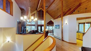 Een ruim interieur met een hoge plafond, houten balken, een gebogen trap en grote ramen met uitzicht.