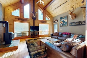 Ein rustikales Blockhaus-Interieur mit Kamin, Ledersofa, aufgehängten Tierköpfen und einem Fernseher.