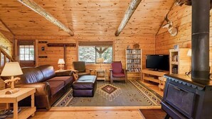 A log cabin interior with a fireplace, leather sofa, armchairs, a TV, and a bookshelf. - Dog-Friendly Cabin w/ Washer/Dryer, WiFi, & Firepit - Steps From the Rio Grande (South Fork)